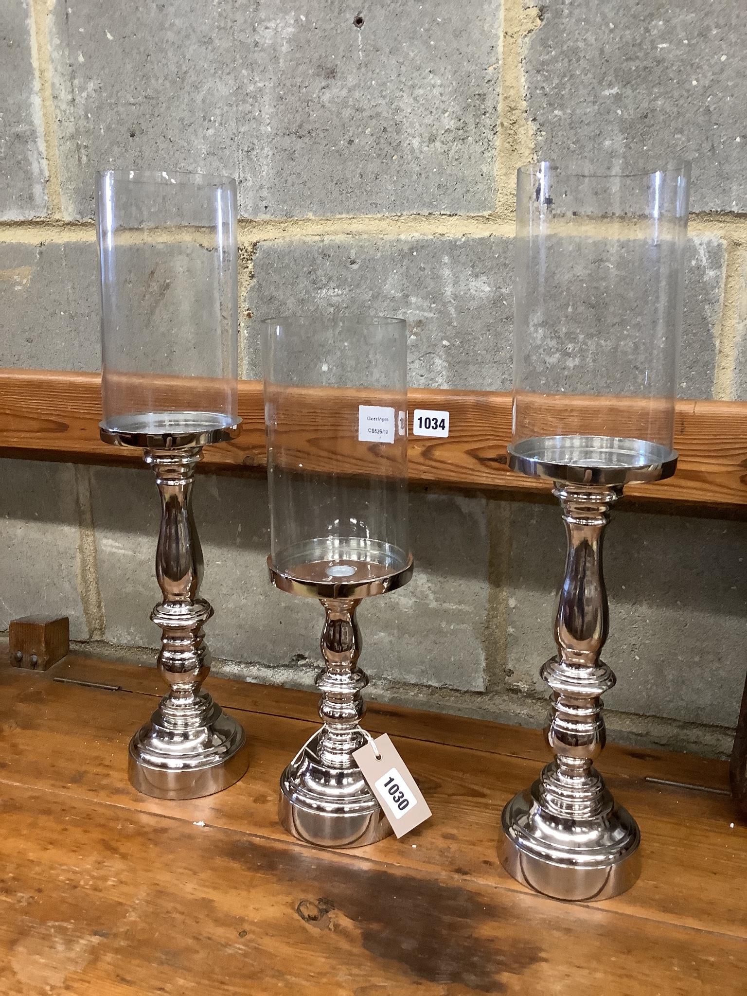 Set of three nickel plated candle stands with glass shades, height 51cm